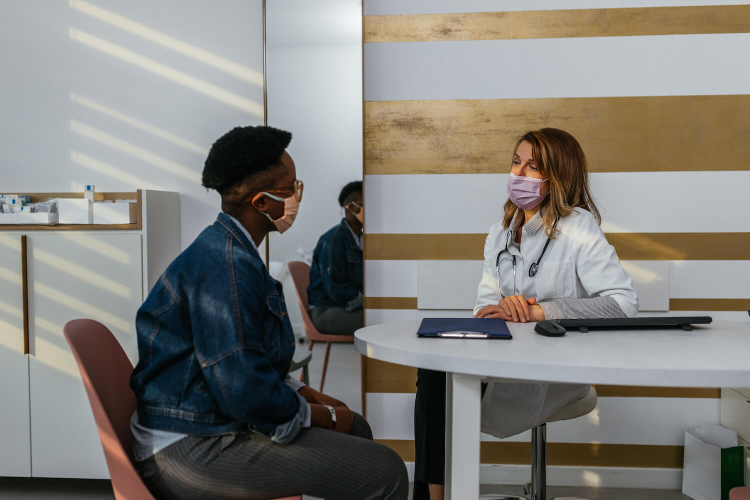 Black patient converses with white healthcare professional in a clinical setting.