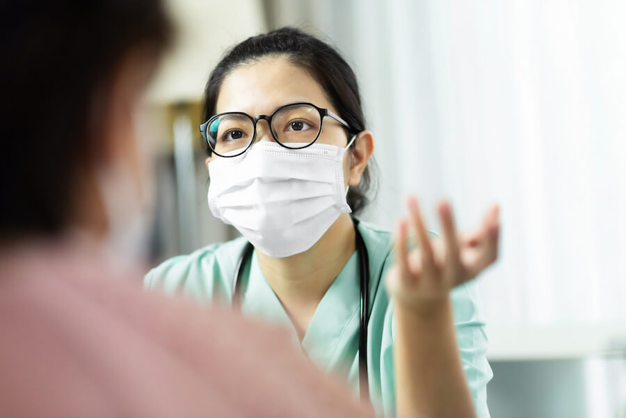 Asian woman Doctor in green uniform wear eyeglasses and surgical mask talking consulting and giving advice to Elderly female patient at the hospital